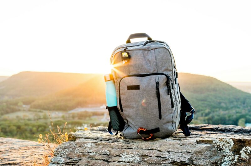 grey and black hiking backpack and cyan tumbler on grey rock during sunset