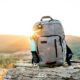 grey and black hiking backpack and cyan tumbler on grey rock during sunset