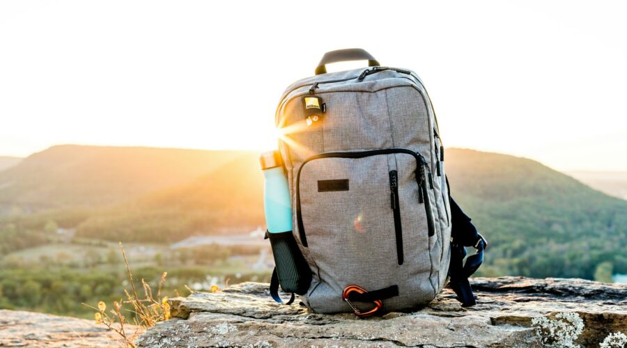 grey and black hiking backpack and cyan tumbler on grey rock during sunset