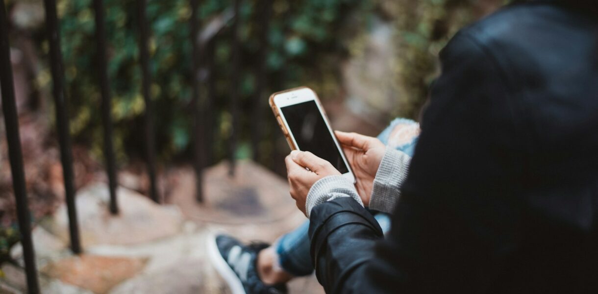 person holding white smartphone sitting on stair