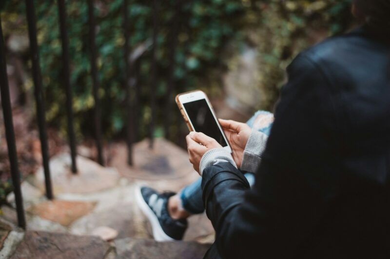 person holding white smartphone sitting on stair