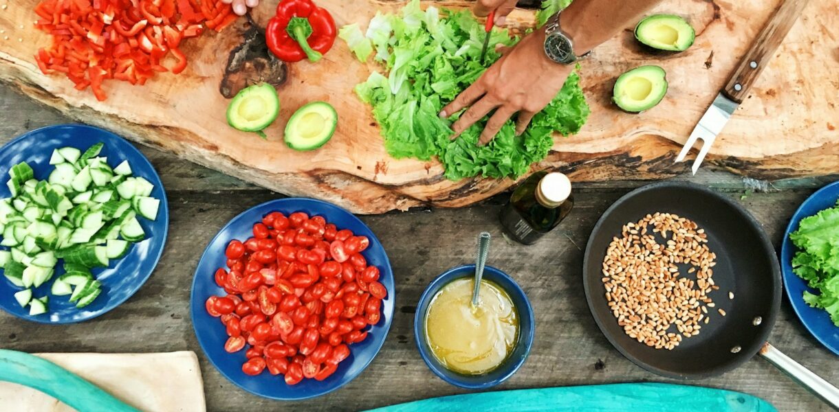 person slicing green vegetable in front of round ceramic plates with assorted sliced vegetables during daytime