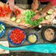 person slicing green vegetable in front of round ceramic plates with assorted sliced vegetables during daytime