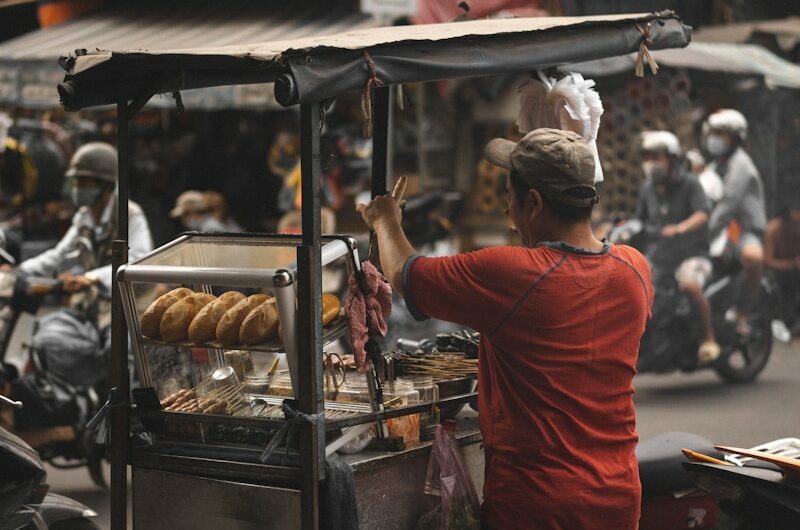 man in red t-shirt and black pants standing in front of food stall during daytime