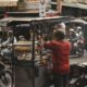 man in red t-shirt and black pants standing in front of food stall during daytime