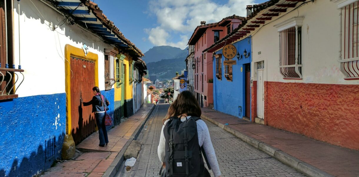 person in gray shirt with backpack walking on street between houses