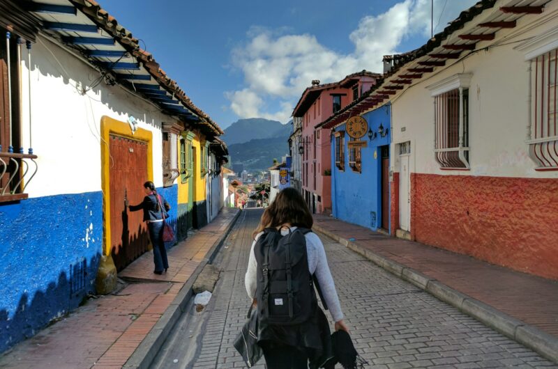 person in gray shirt with backpack walking on street between houses