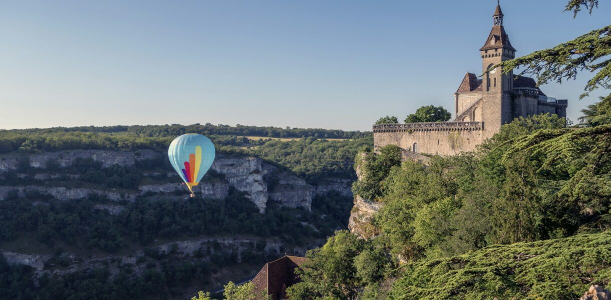 a hot air balloon flying over a hill with trees and a castle