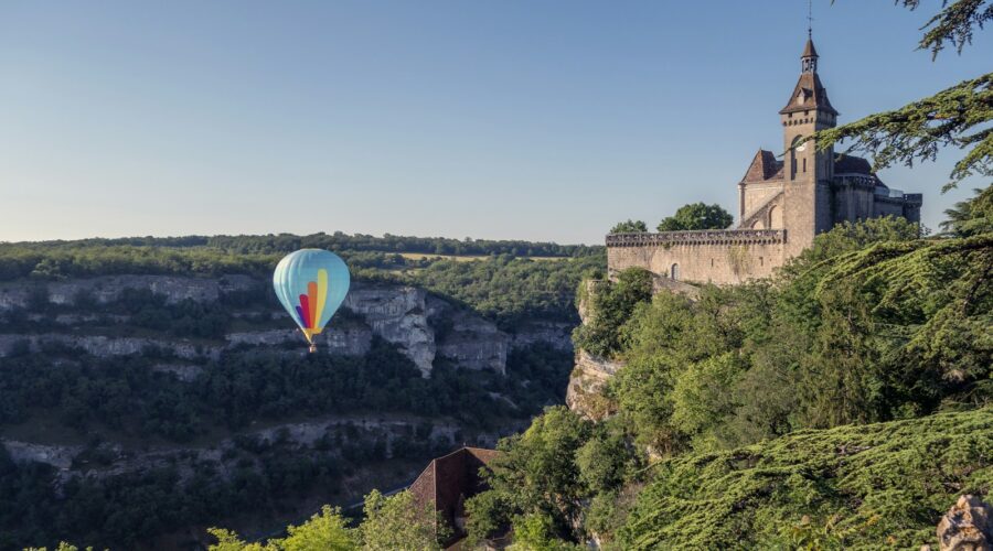 a hot air balloon flying over a hill with trees and a castle