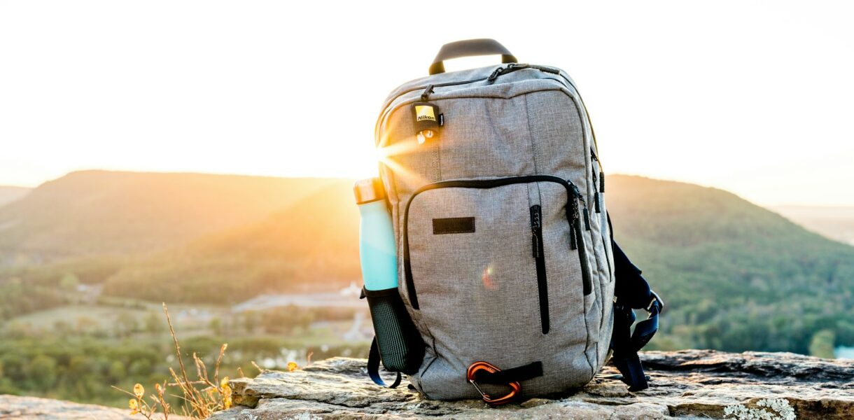 grey and black hiking backpack and cyan tumbler on grey rock during sunset